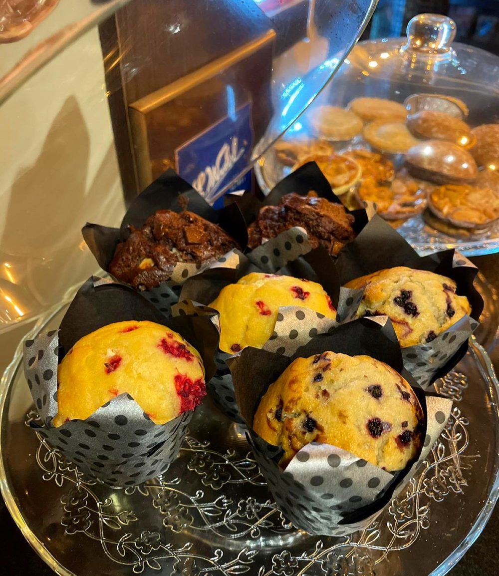 A tray of freshly baked muffins in dark paper cases under the counter glass
