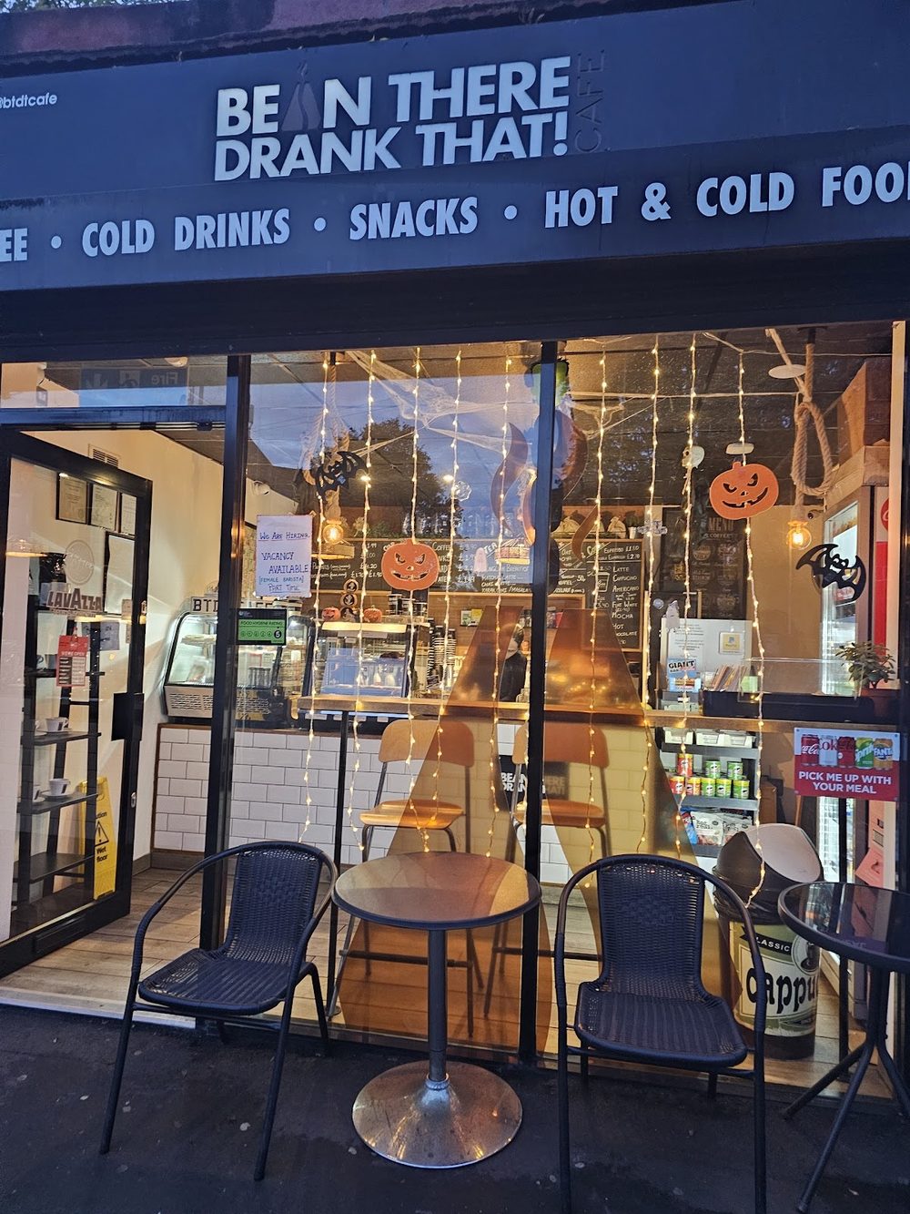 The cafe shopfront at dusk, fairy lights in the window and a small table for two on the pavement